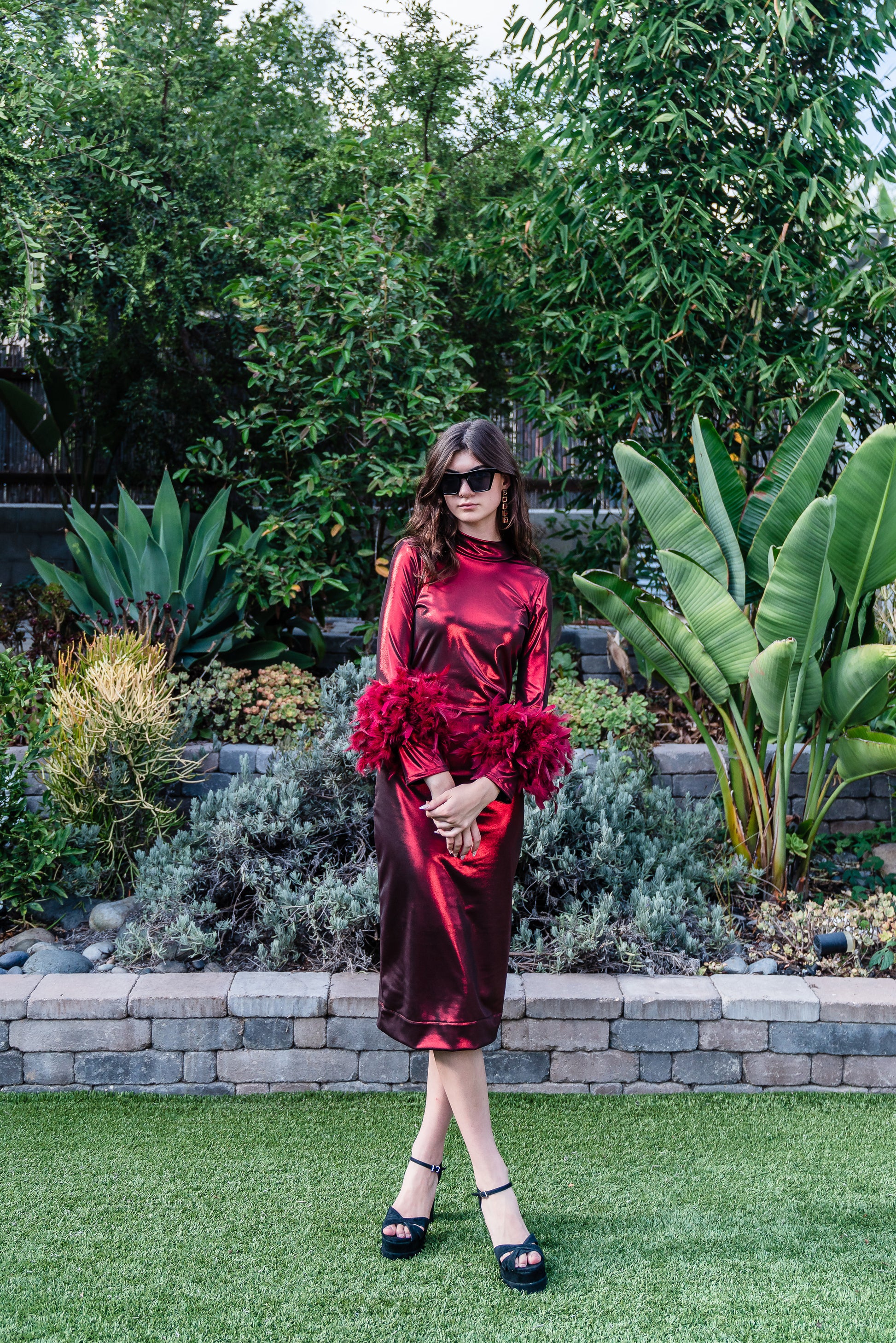 This cherry lamé, bodycon dress accentuates your curves, while the removable feather trim on the sleeves adds a touch of elegance.