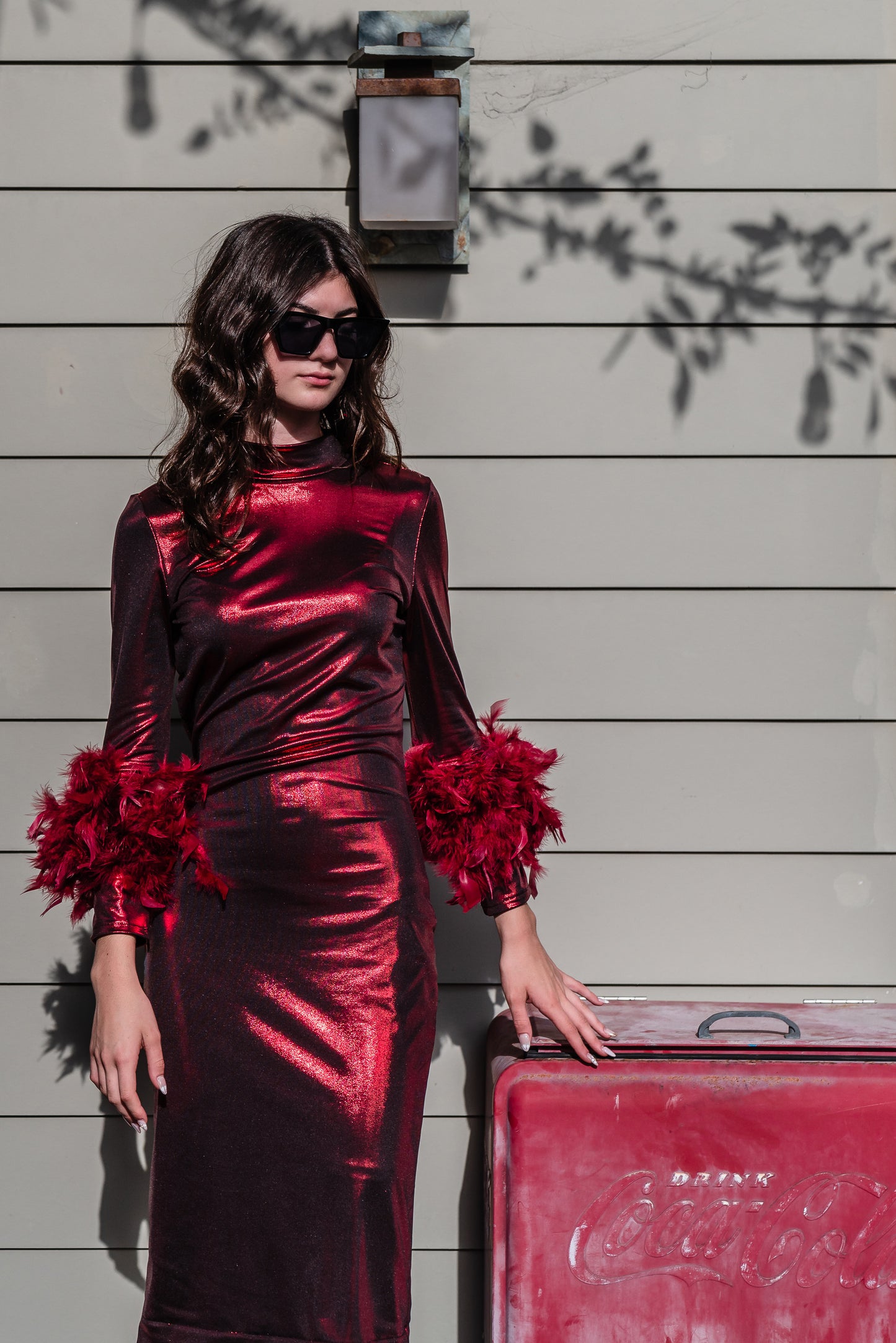 This cherry lamé, bodycon dress accentuates your curves, while the removable feather trim on the sleeves adds a touch of elegance.