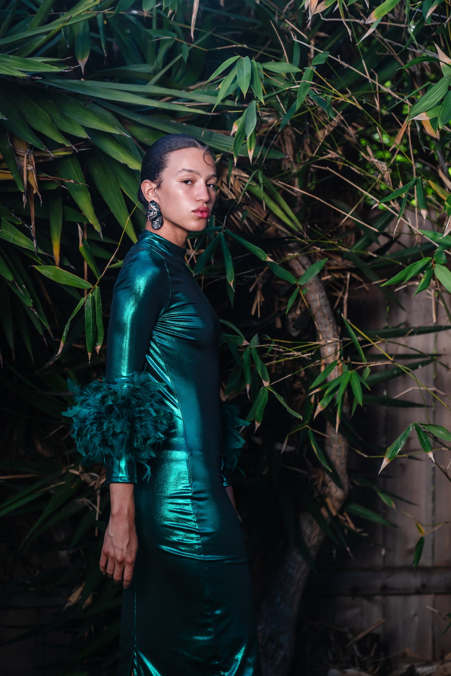 This emerald lamé, bodycon dress accentuates your curves, while the removable feather trim on the sleeves adds a touch of elegance.