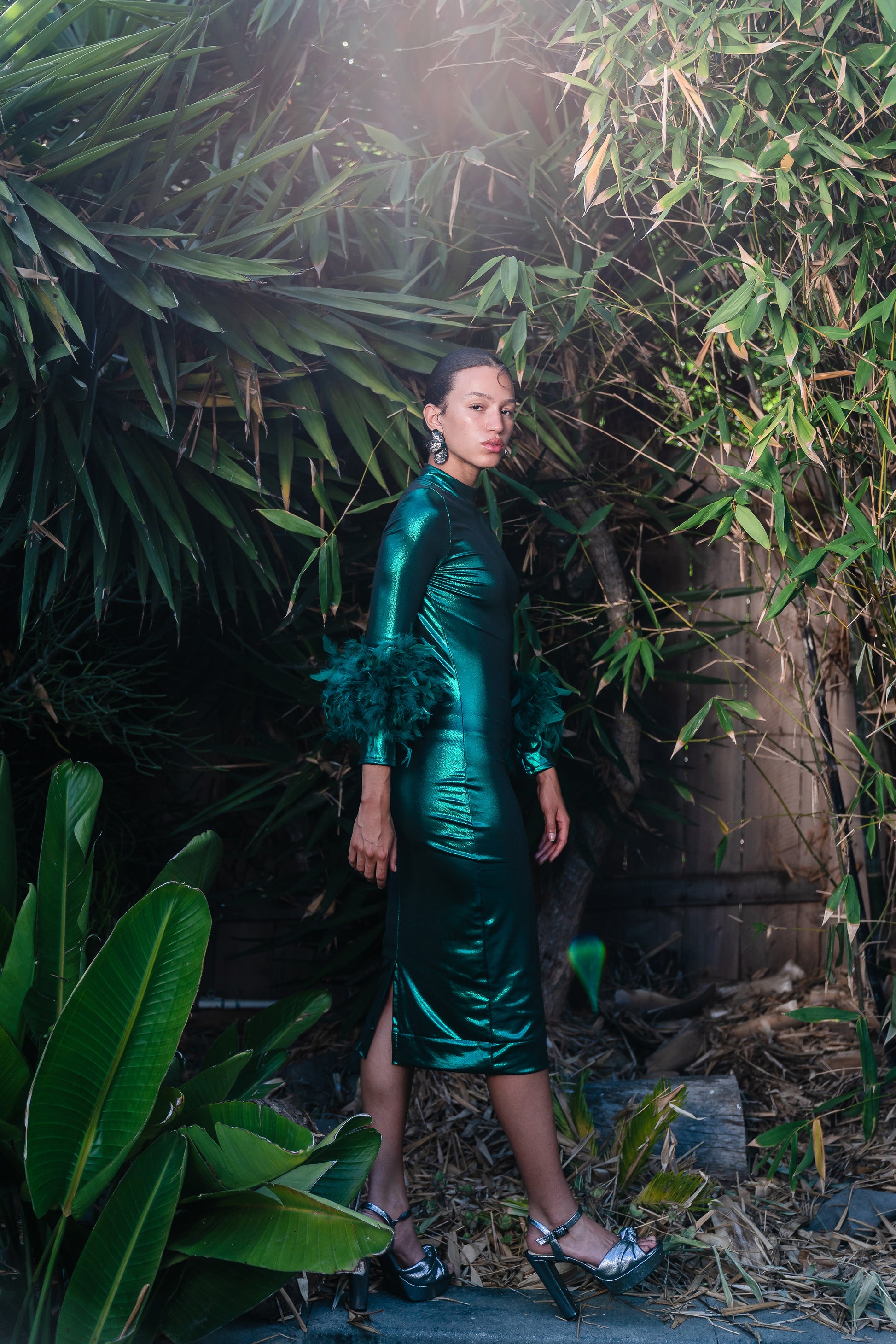 This emerald lamé, bodycon dress accentuates your curves, while the removable feather trim on the sleeves adds a touch of elegance.