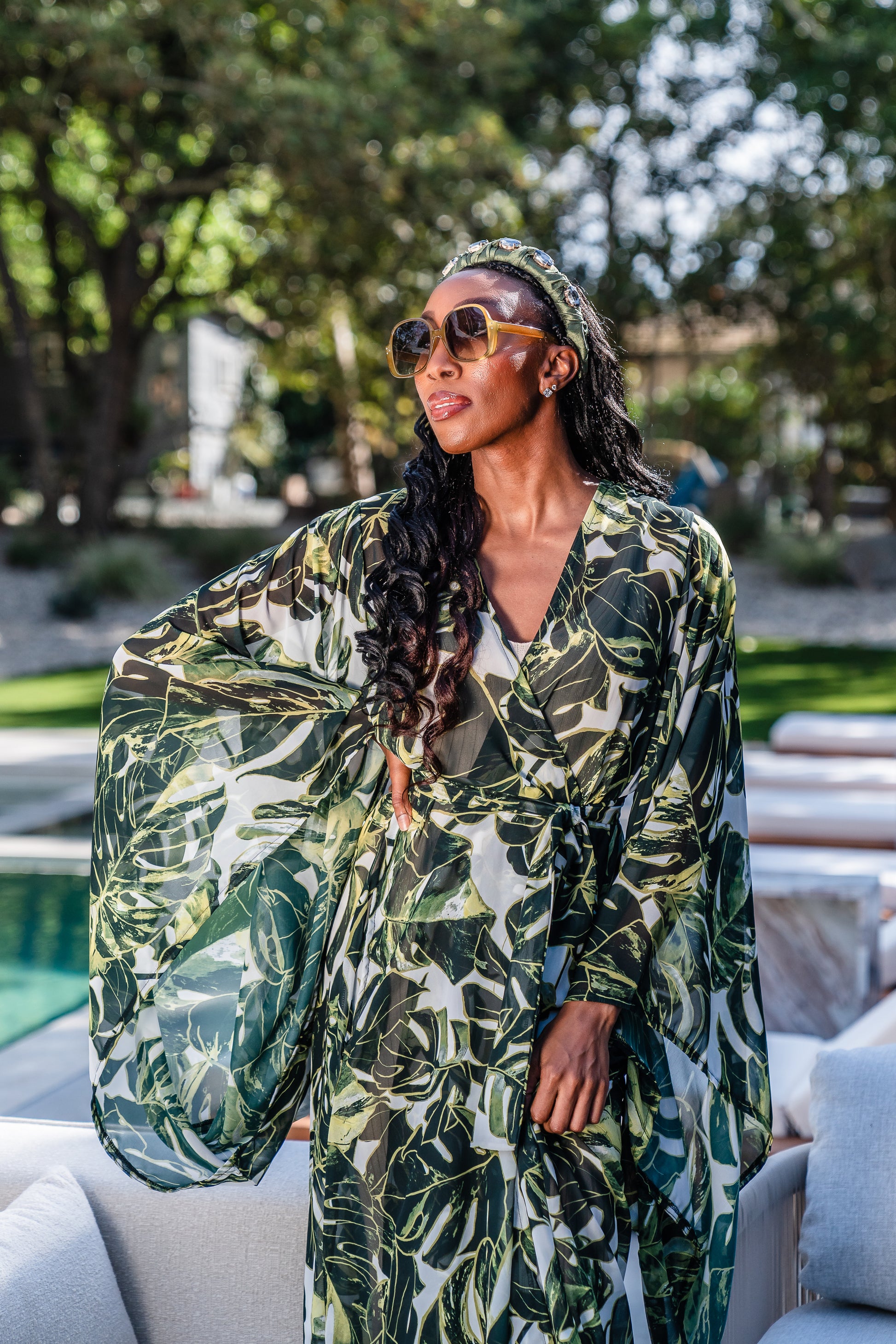 Model wears white chiffon Kimono with varying green palm leaf print. The kimono has classic wide kimono sleeves and lands at midi length. Kimono has a matching tie belt.