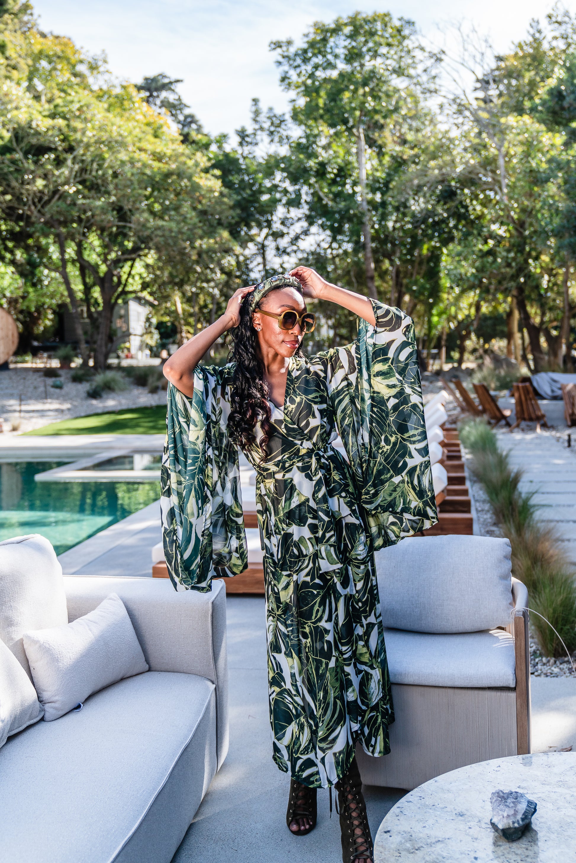 Model wears white chiffon Kimono with varying green palm leaf print. The kimono has classic wide kimono sleeves and lands at midi length. Kimono has a matching tie belt.