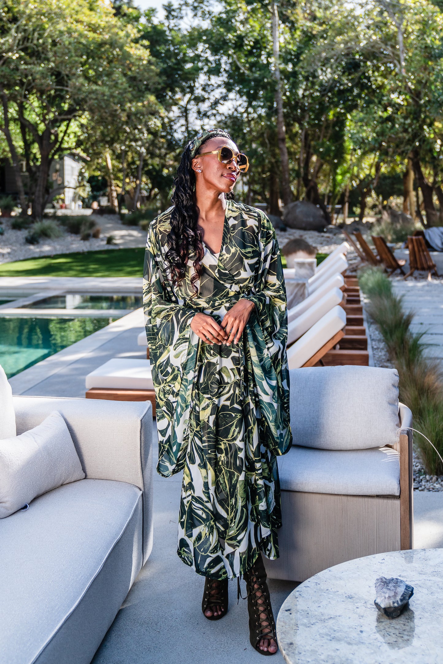 Model wears white chiffon Kimono with varying green palm leaf print. The kimono has classic wide kimono sleeves and lands at midi length. Kimono has a matching tie belt.