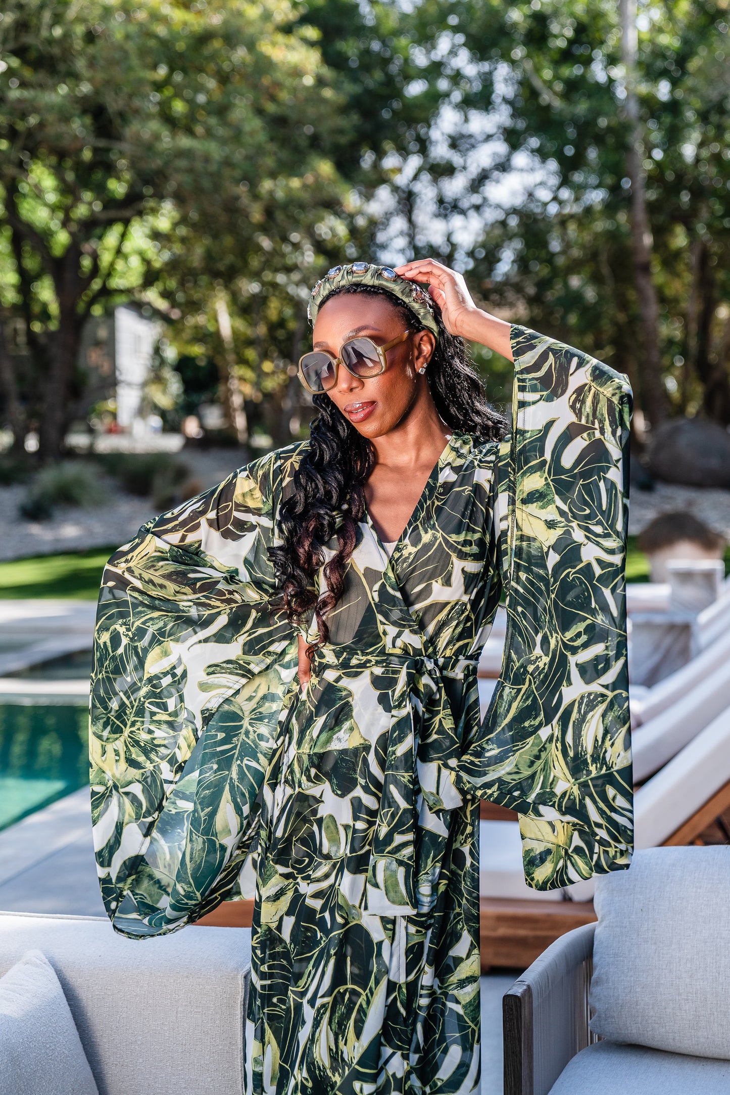 Model wears white chiffon Kimono with varying green palm leaf print. The kimono has classic wide kimono sleeves and lands at midi length. Kimono has a matching tie belt.