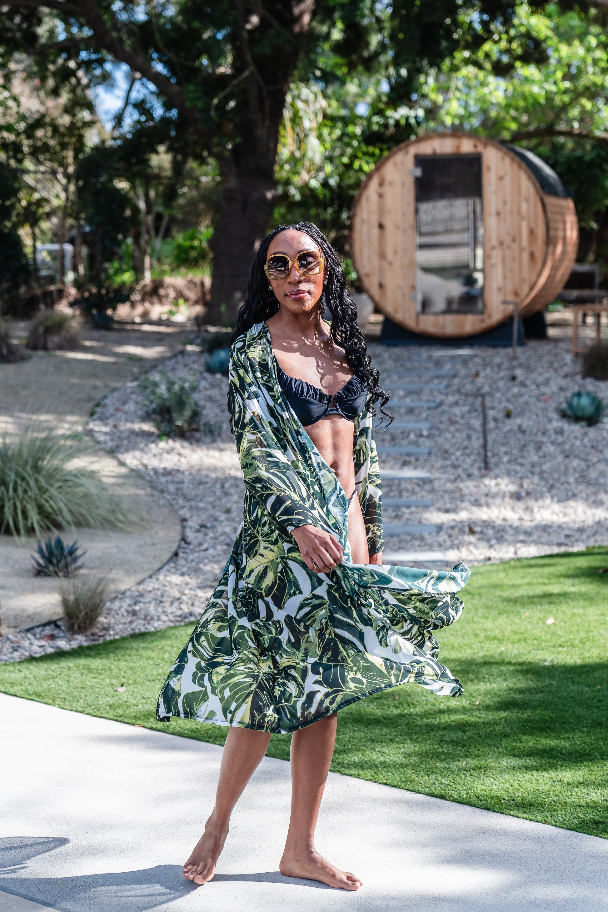 Model wears white chiffon Kimono with varying green palm leaf print. The kimono has classic wide kimono sleeves and lands at midi length. Kimono has a matching tie belt.