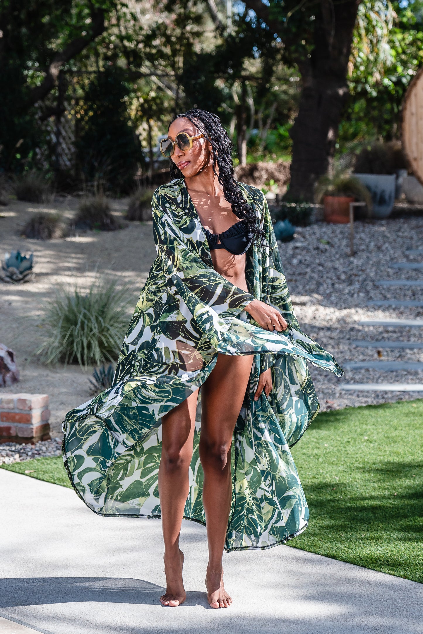 Model wears white chiffon Kimono with varying green palm leaf print. The kimono has classic wide kimono sleeves and lands at midi length. Kimono has a matching tie belt.
