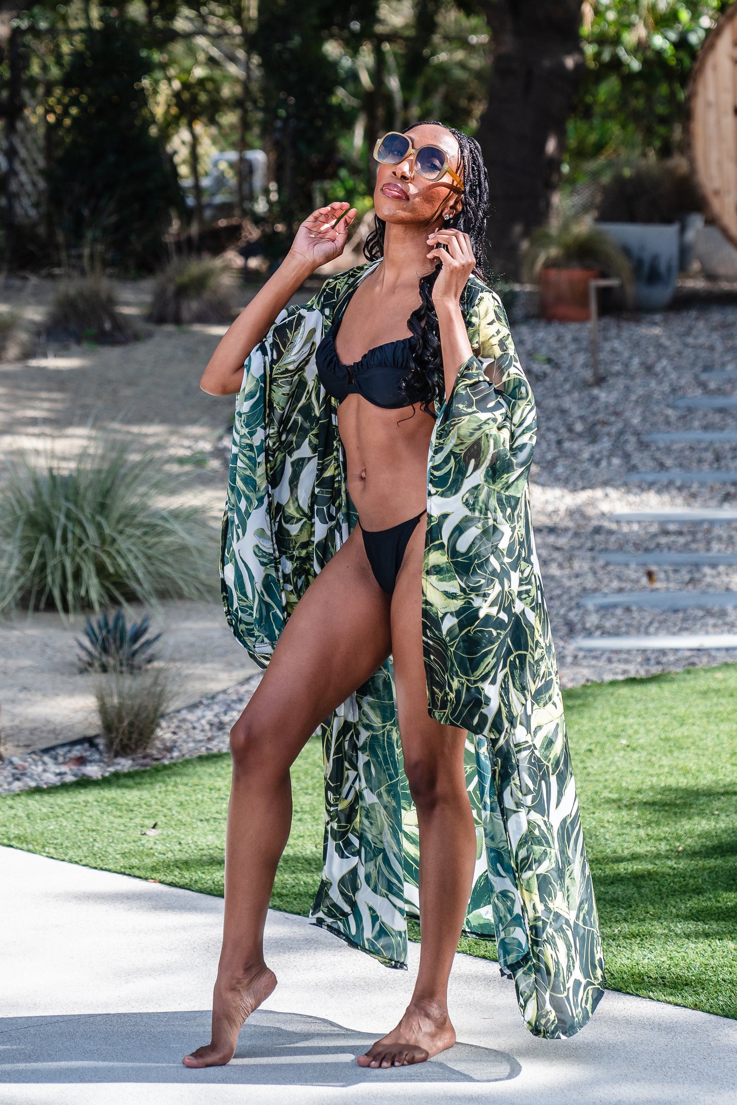 Model wears white chiffon Kimono with varying green palm leaf print. The kimono has classic wide kimono sleeves and lands at midi length. Kimono has a matching tie belt.