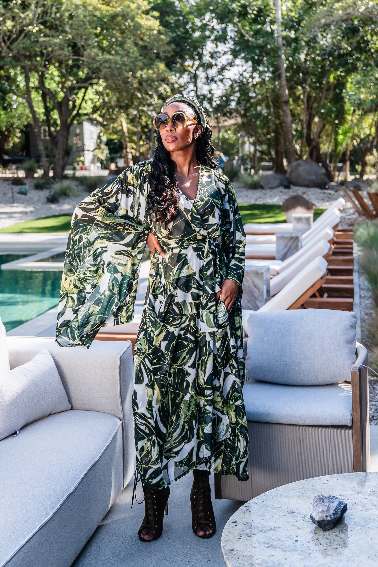 Model wears white chiffon Kimono with varying green palm leaf print. The kimono has classic wide kimono sleeves and lands at midi length. Kimono has a matching tie belt.