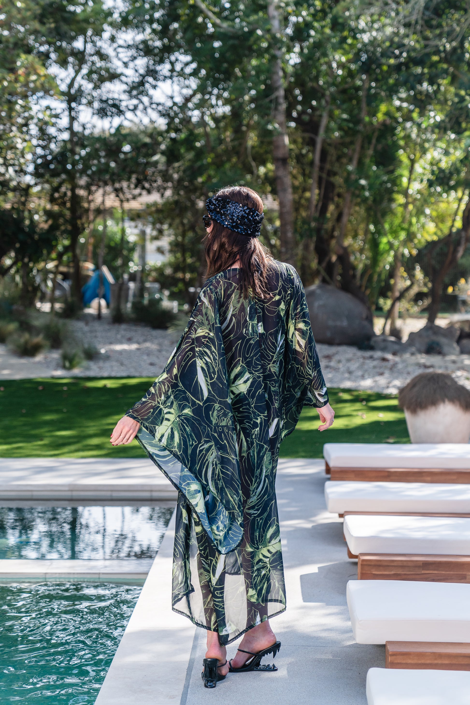 Model wears black chiffon Kimono with varying green palm leaf print. The kimono has classic wide kimono sleeves and lands at midi length. Kimono has a matching tie belt.