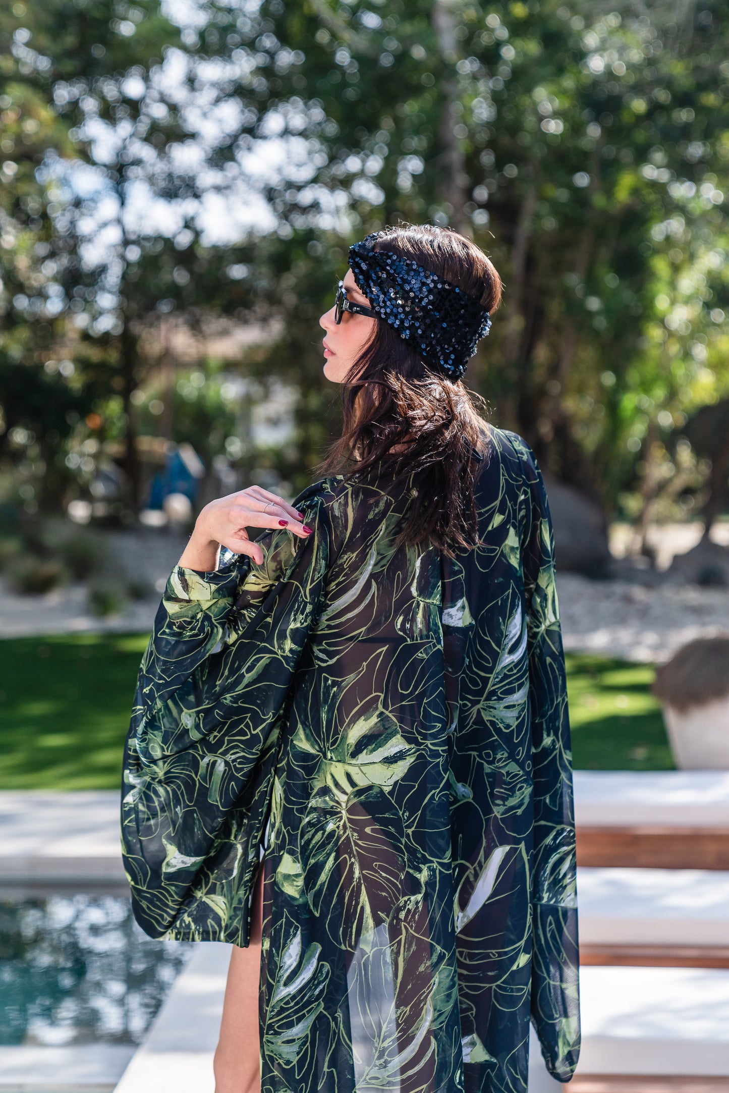 Model wears black chiffon Kimono with varying green palm leaf print. The kimono has classic wide kimono sleeves and lands at midi length. Kimono has a matching tie belt.