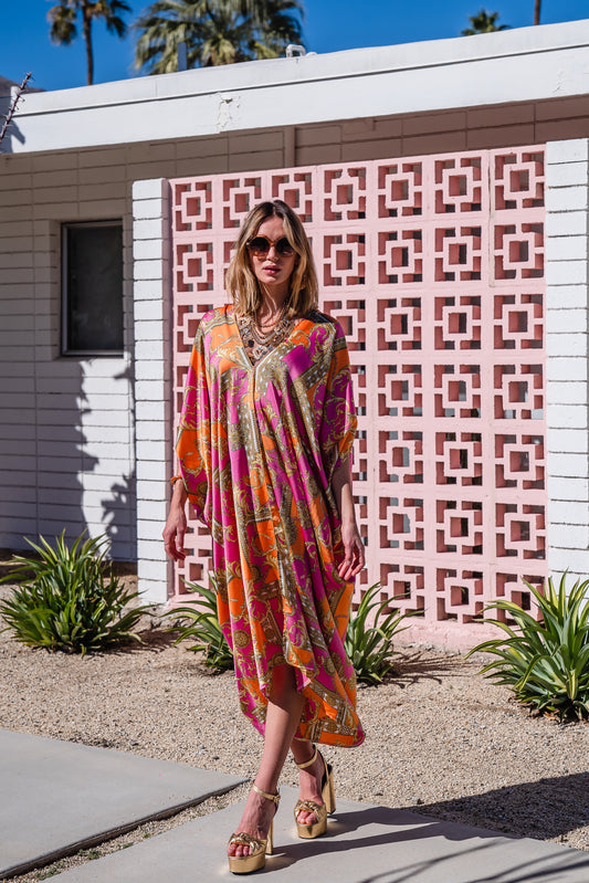 Jennafer Grace Voglia Rosa caftan. Featuring an orange, pink, and gold baroque pattern, deep v-neckline, ankle length hem, and batwing sleeves. 