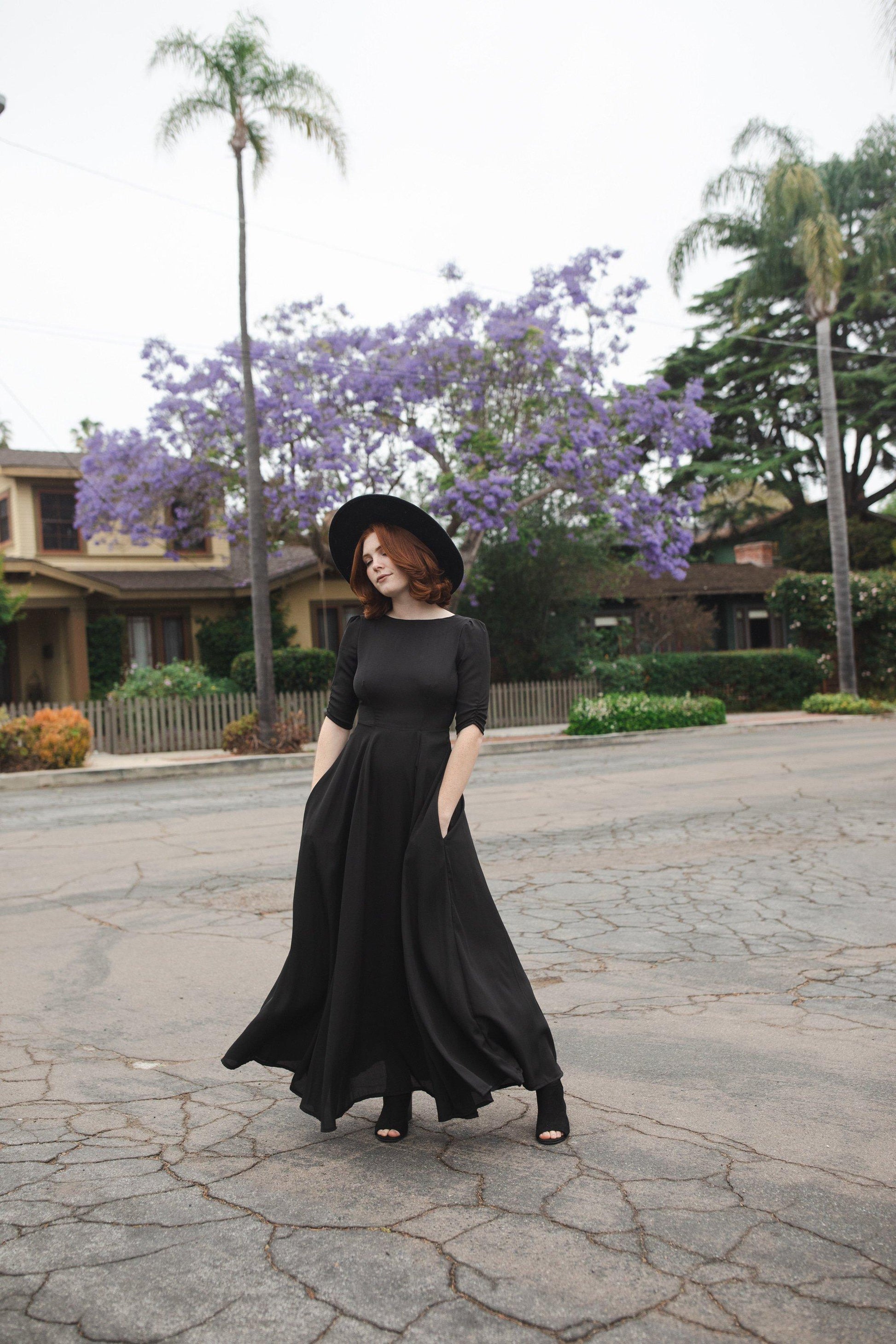 Jennafer Grace solid black maxi dress features princess seamed skirts and pockets. The dress has an invisible zipper and high/low neck options you can wear it multiple ways. Fitted torso with elbow length sleeves and ankle hem.