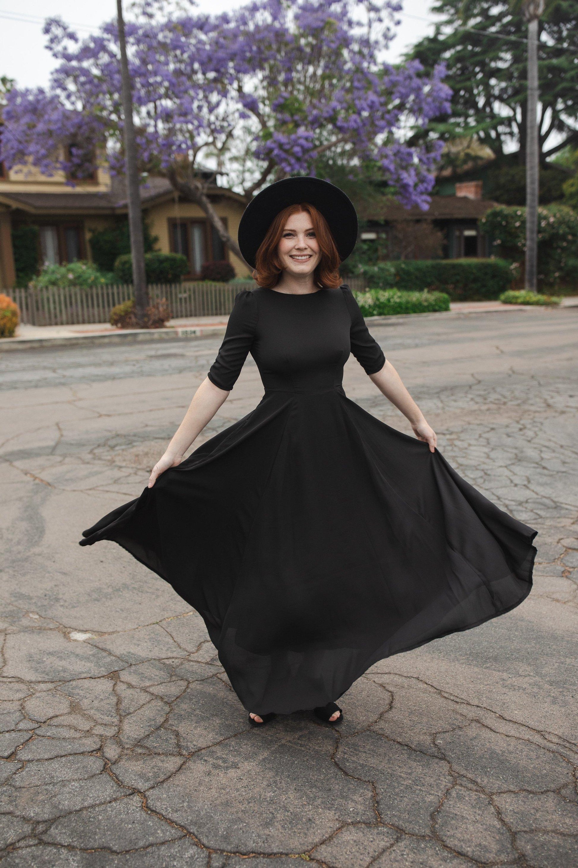 Jennafer Grace solid black maxi dress features princess seamed skirts and pockets. The dress has an invisible zipper and high/low neck options you can wear it multiple ways. Fitted torso with elbow length sleeves and ankle hem. 