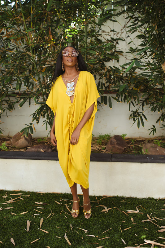 Vibrant yellow caftan. This piece features a deep v-neck, batwing sleeve, a center drawstring for ruche styling, and ankle length hem. Retro bohemian aesthetic.