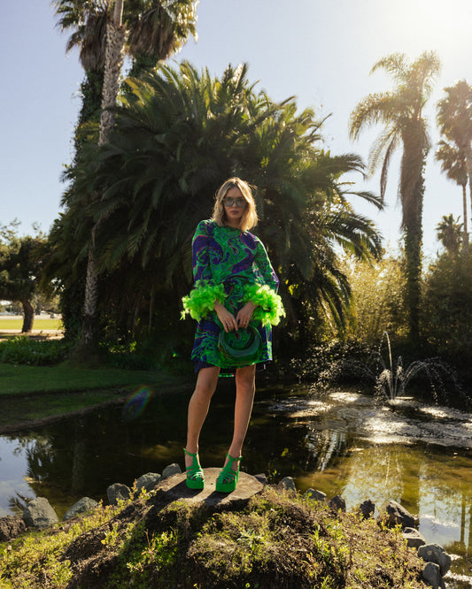 Funky fresh retro midi dress with royal blue and lime green abstract filigree swirl print with hints of aqua and fuchsia. The dress features a crew neck, keyhole detail at upper back, 3/4 bell sleeves with neon green feathers at cuff, a knee-length hem, and optional wrap tie for a cinched waist.
