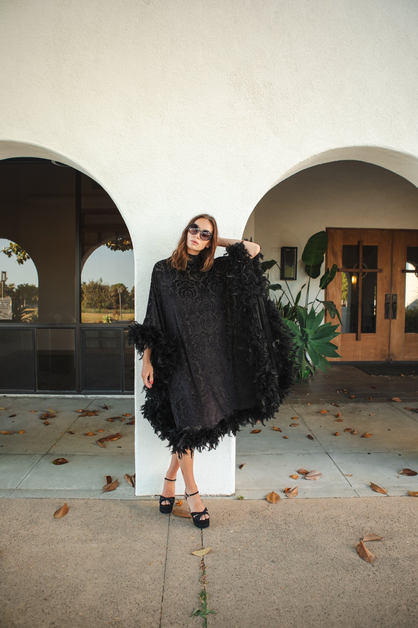 The Black Widow Mockneck Feather Caftan with slip. A darkly romantic, semi-sheer, black stretch velvet kaftan with a vintage-inspired, ornamental burnout pattern and soft black feather border along sleeves and hem. A gothic bohemian dress inspired by Old Hollywood glam.