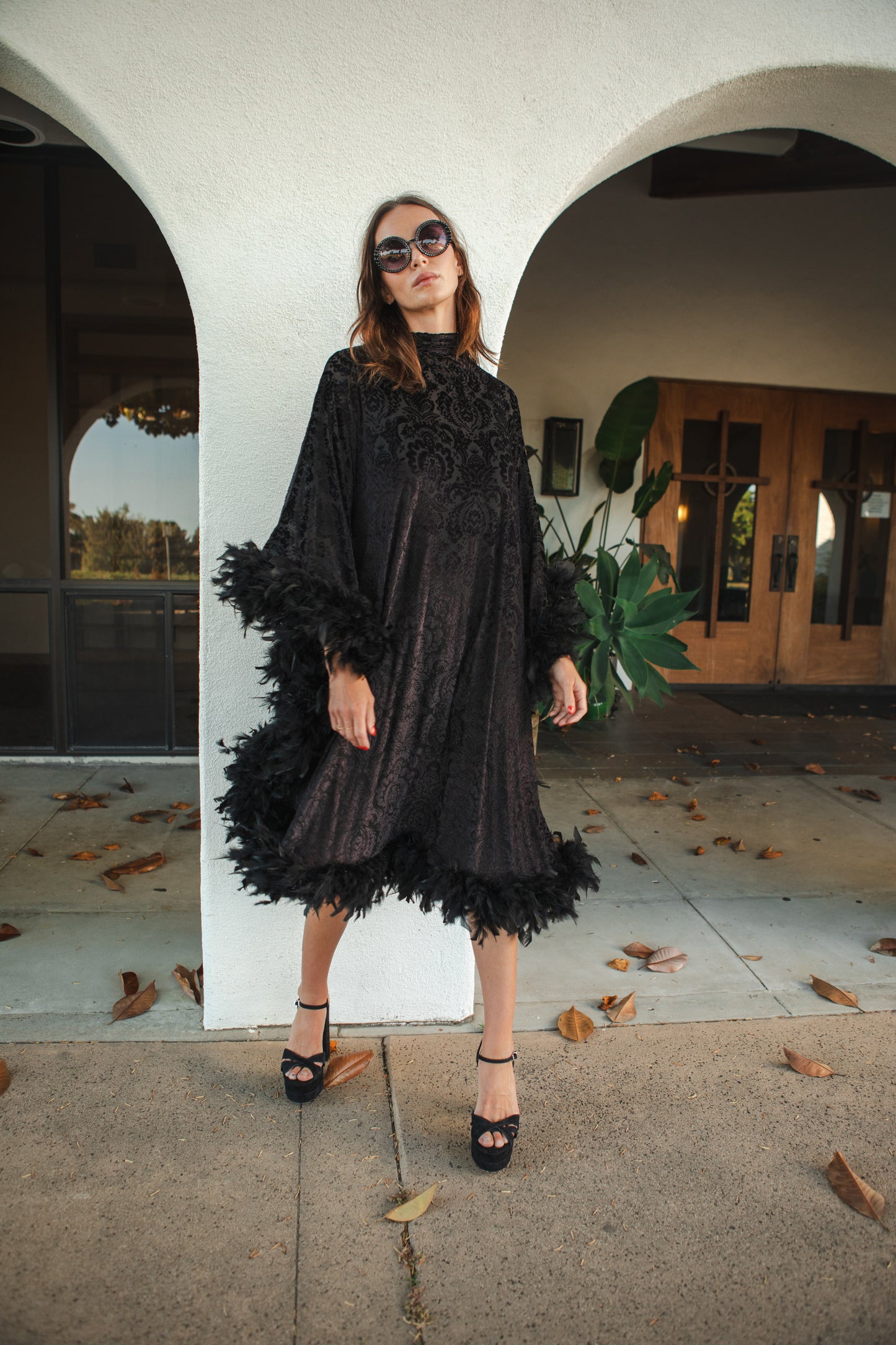 The Black Widow Mockneck Feather Caftan with slip. A darkly romantic, semi-sheer, black stretch velvet kaftan with a vintage-inspired, ornamental burnout pattern and soft black feather border along sleeves and hem. A gothic bohemian dress inspired by Old Hollywood glam.