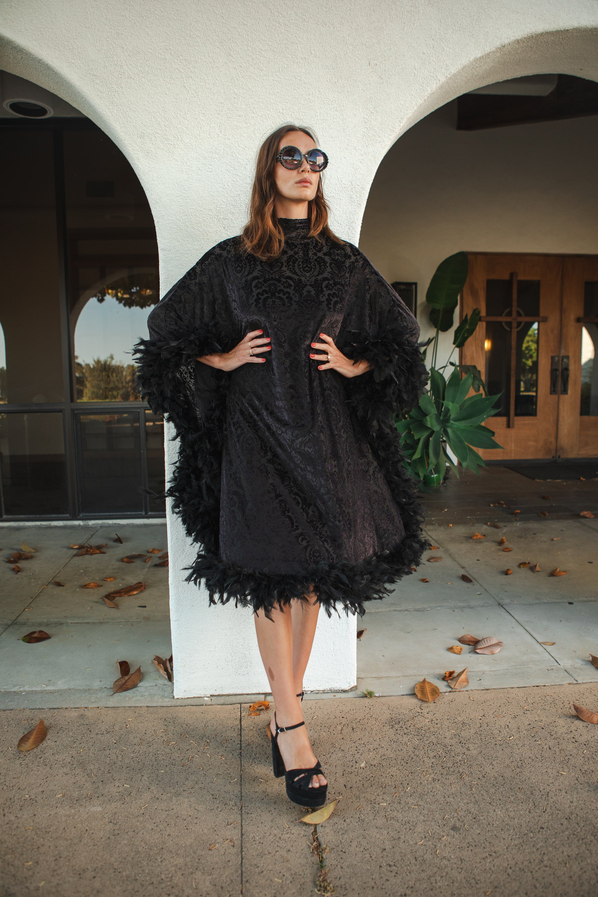 The Black Widow Mockneck Feather Caftan with slip. A darkly romantic, semi-sheer, black stretch velvet kaftan with a vintage-inspired, ornamental burnout pattern and soft black feather border along sleeves and hem. A gothic bohemian dress inspired by Old Hollywood glam.
