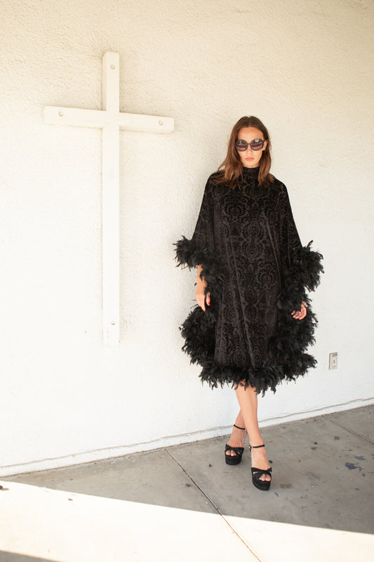 The Black Widow Mockneck Feather Caftan with slip. A darkly romantic, semi-sheer, black stretch velvet kaftan with a vintage-inspired, ornamental burnout pattern and soft black feather border along sleeves and hem. A gothic bohemian dress inspired by Old Hollywood glam.