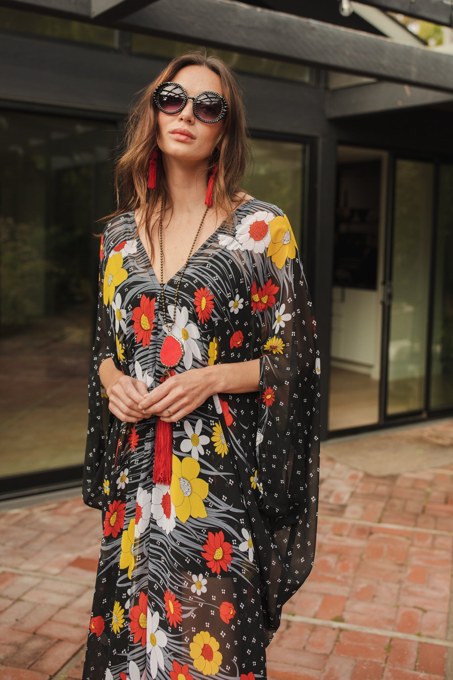 Flowy chiffon caftan with whimsical daisy print. Base color is black with a mixture of orange, white, and yellow floral patterns. Features a v-neck, batwing sleeves, and ankle hem.