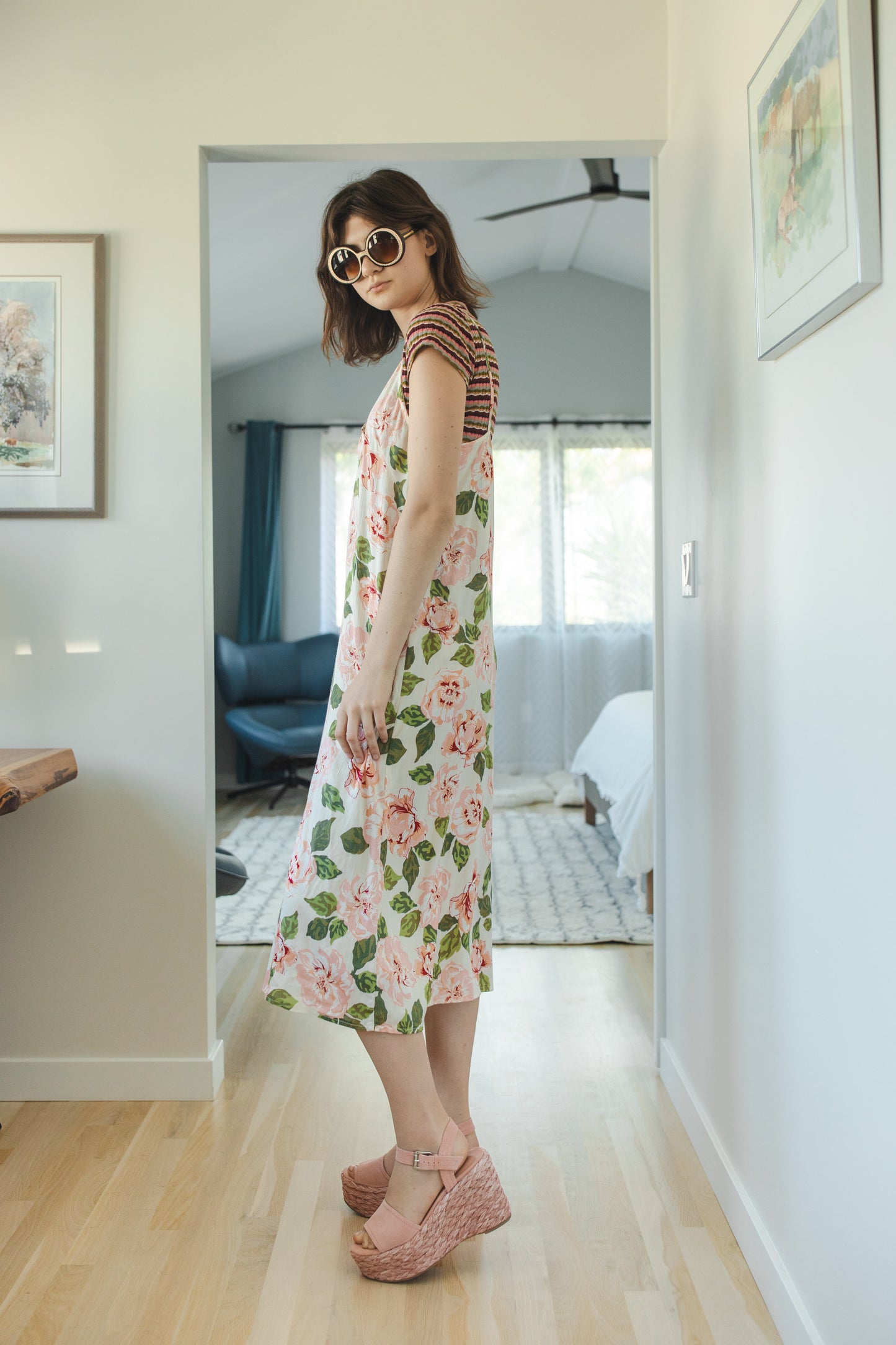 Midi slip dress with an ivory base color, adorned with floral rose print pattern featuring shades of green and pink. It features slender straps with a straight silhouette and relaxed fix, allowing for a beautiful drape and flowy movement. It's designed for a light, airy feel, suitable for warm weather or layered for cooler days.