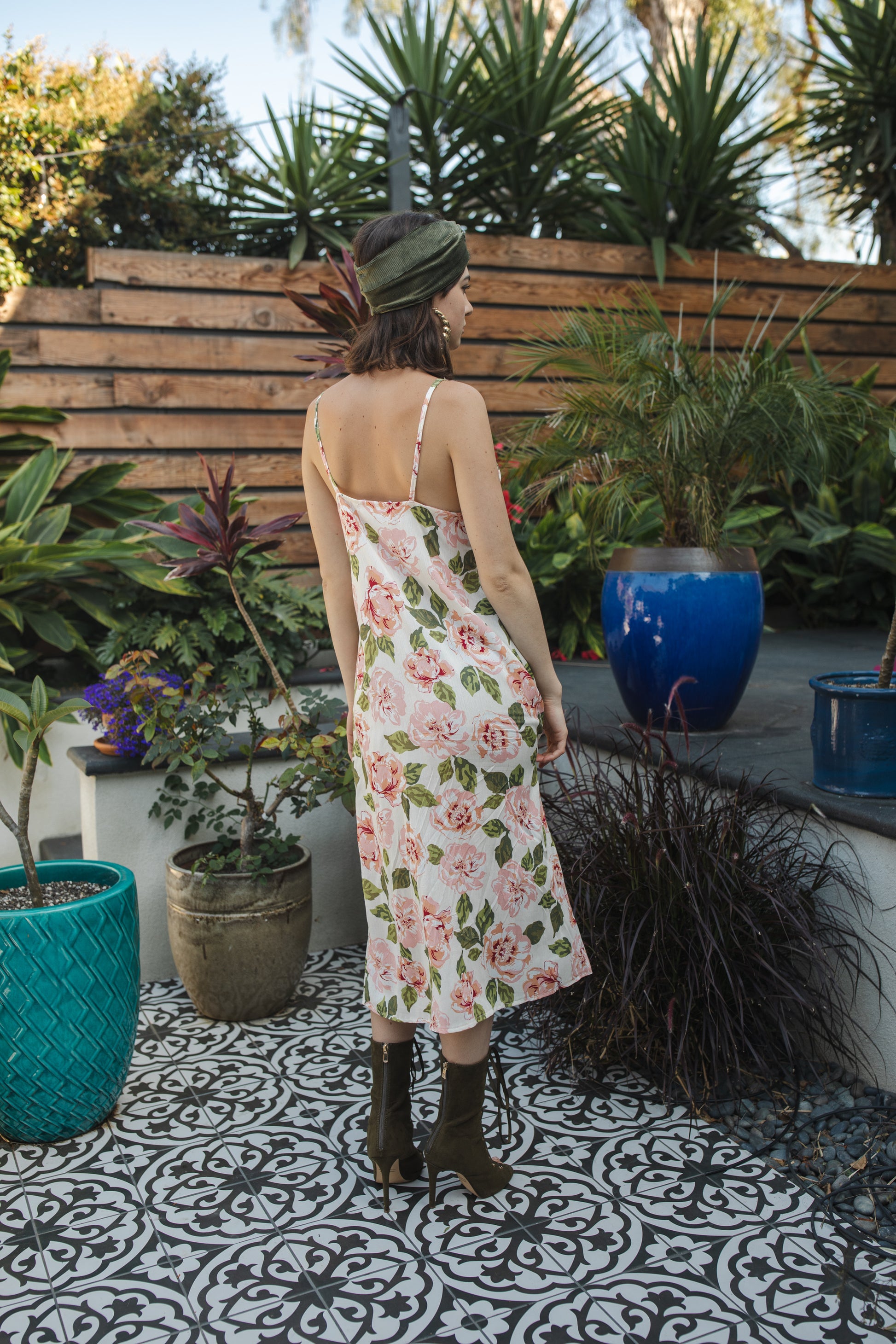 Midi slip dress with an ivory base color, adorned with floral rose print pattern featuring shades of green and pink. It features slender straps with a straight silhouette and relaxed fix, allowing for a beautiful drape and flowy movement. It's designed for a light, airy feel, suitable for warm weather or layered for cooler days.