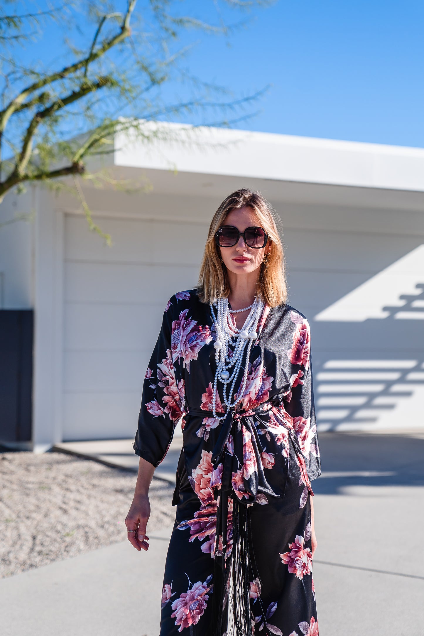 Loungewear set in dark floral pattern. A black background with light pink flowers, this set comes with a wrap dolman jacket.  Sleeves have a forearm hem, and it can be worn as an open jacket or wrap with matching tie belt. The belt features fringe tassels. The matching pants have pockets and an ankle length hem. 