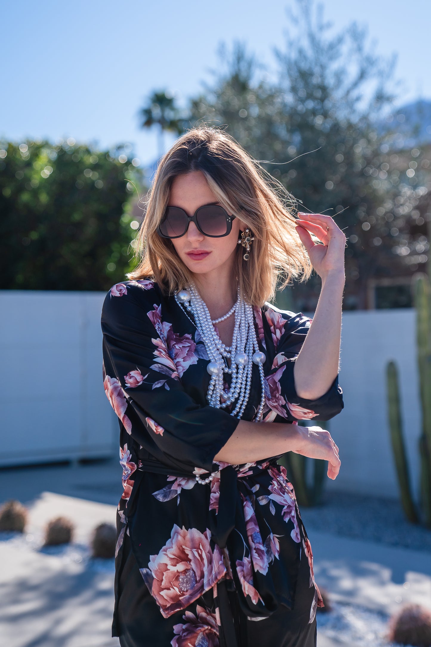 Loungewear set in dark floral pattern. A black background with light pink flowers, this set comes with a wrap dolman jacket.  Sleeves have a forearm hem, and it can be worn as an open jacket or wrap with matching tie belt. The belt features fringe tassels. The matching pants have pockets and an ankle length hem. 