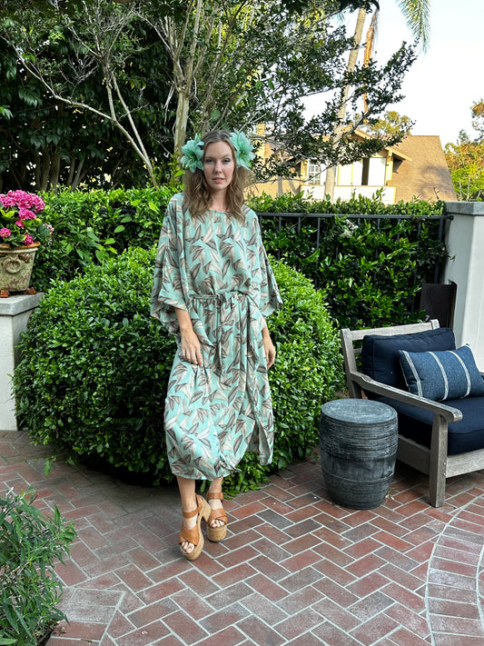 The Menta Dulce Belted Disco caftan dress featuring a mint colored palm print, batwing sleeves, boat neck, ankle hem, and optional belt to promote a flattering silhouette.