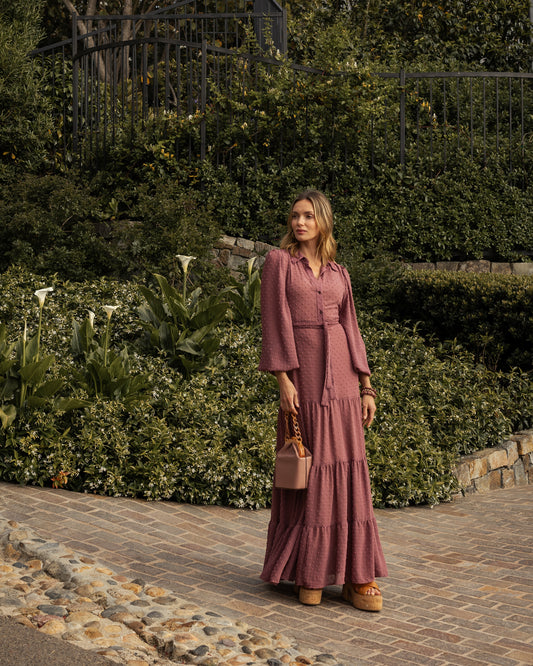 This Swiss Dot maxi dress is sophisticated yet effortless with its high collar, button-up design paired with bishop sleeves, tiered skirt, and a slim matching sash.