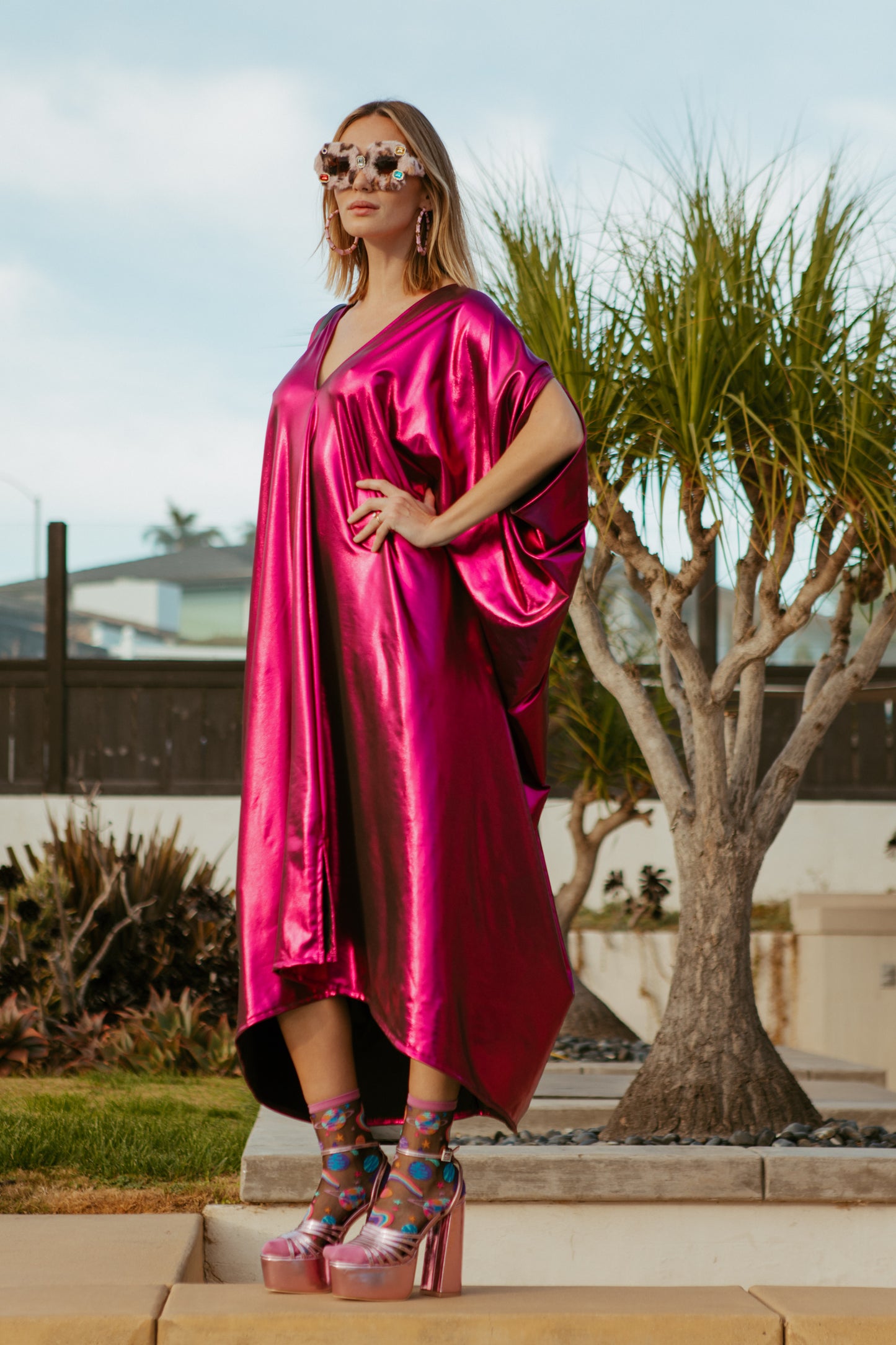Bold, metallic caftan crafted from a slinky black jersey coated with a deep fuchsia foil that shimmers in the light. The caftan has a generous, free-flowing cut, with ample fabric creating an elegant, loose fit that drapes comfortably over the body, with batwing sleeves and a deep v-neckline.