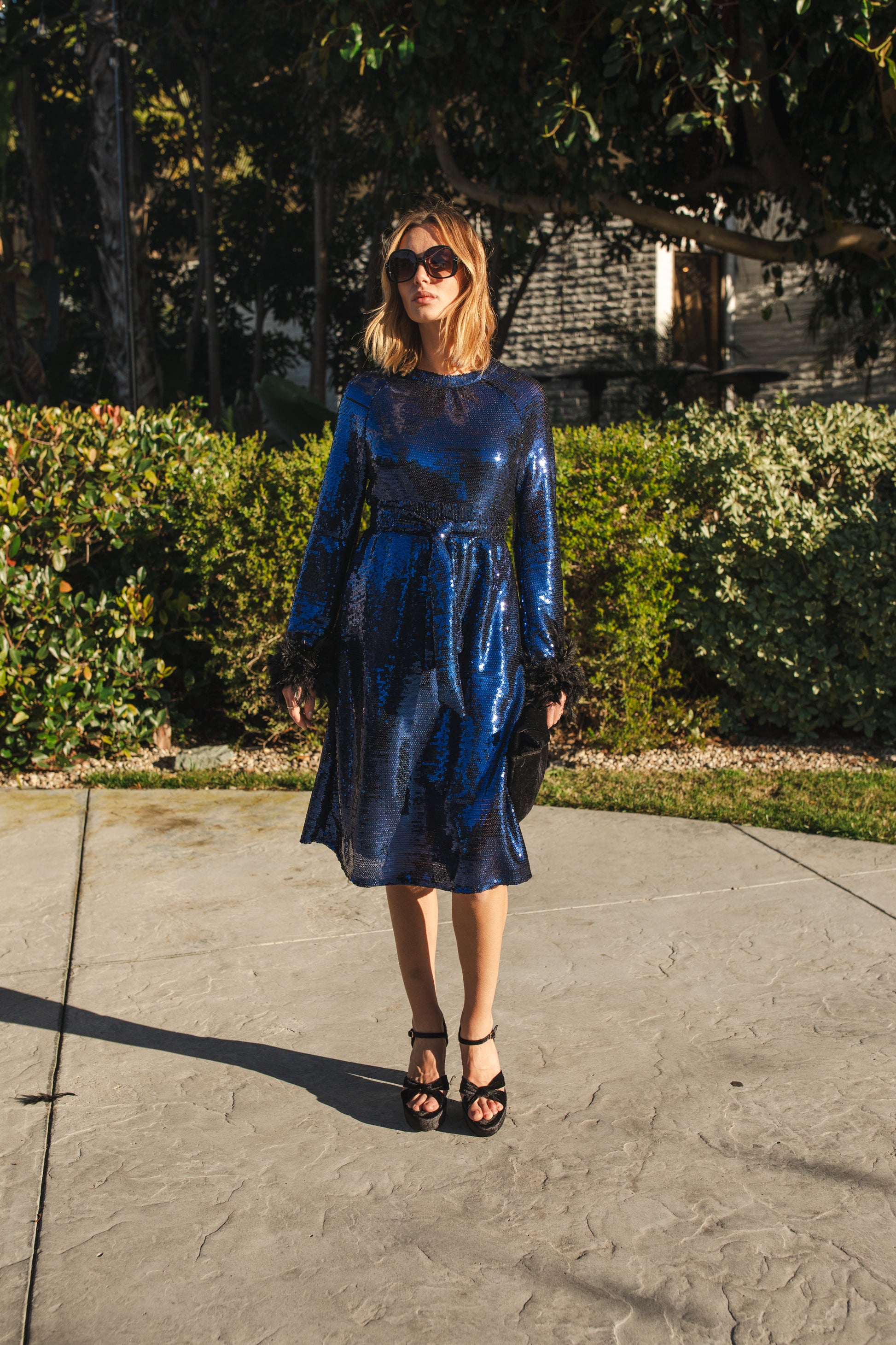 Model wears a knee length dress covered in midnight blue sequins, the dress has a crew neck and full long sleeves with a feather trim.