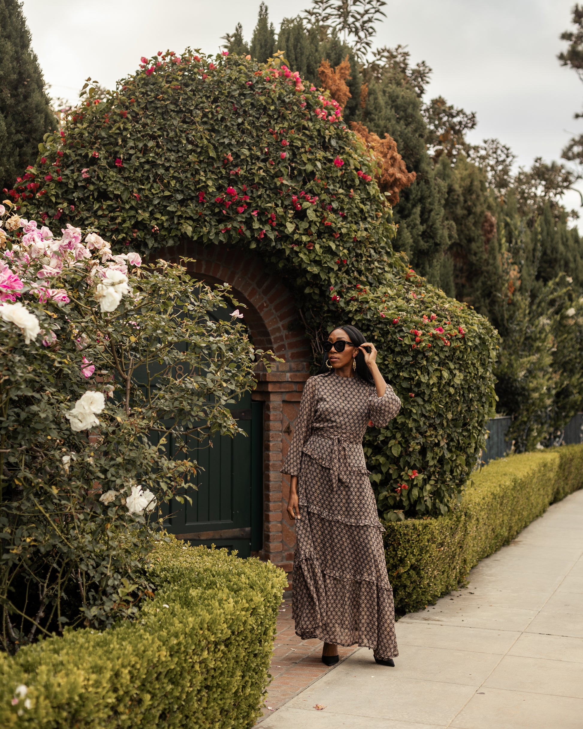 This beige and black floral maxi dress is crafted with a soft, metallic infused fabric, it features high neck, bishop sleeves, tiered ruffle skirt and matching sash for a cinched waist.