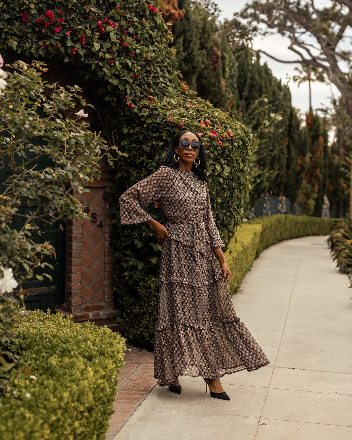 This beige and black floral maxi dress is crafted with a soft, metallic infused fabric, it features high neck, bishop sleeves, tiered ruffle skirt and matching sash for a cinched waist.