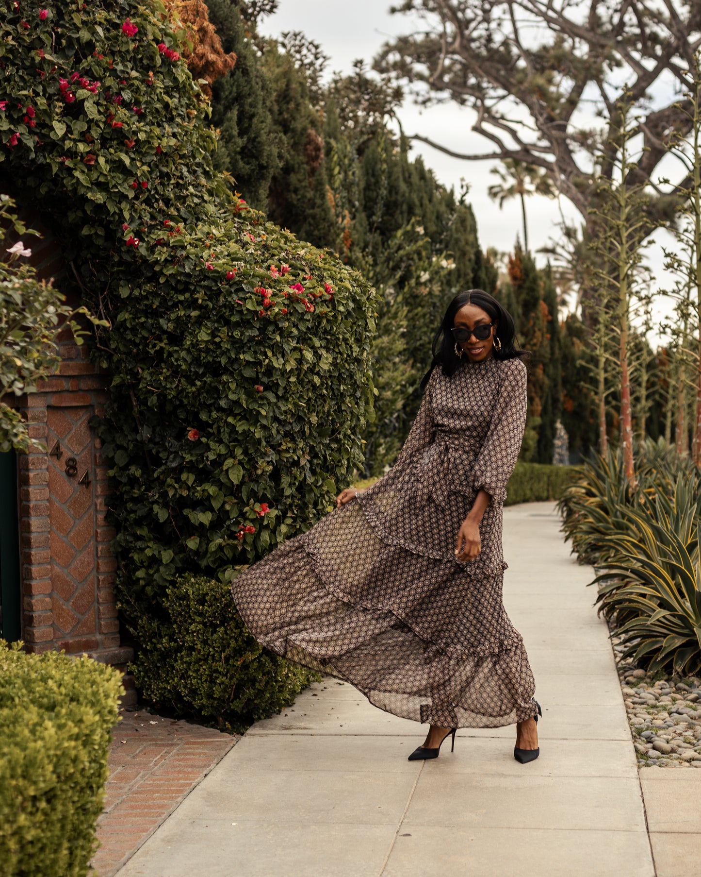 This beige and black floral maxi dress is crafted with a soft, metallic infused fabric, it features high neck, bishop sleeves, tiered ruffle skirt and matching sash for a cinched waist.