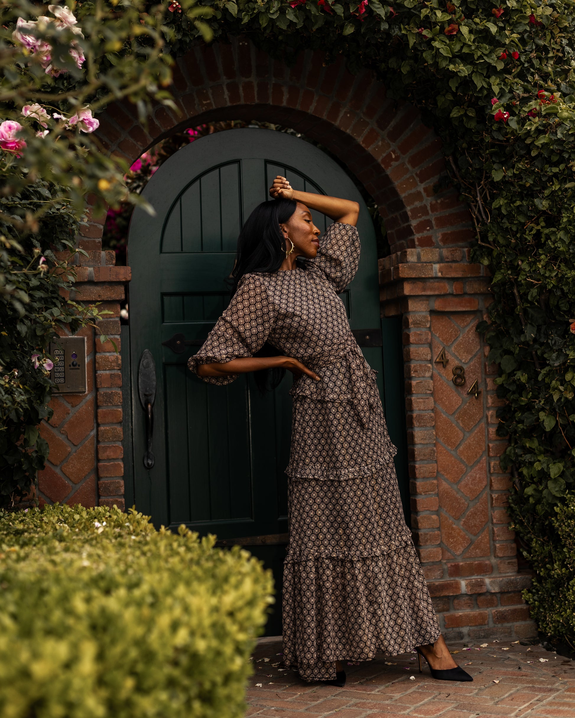 This beige and black floral maxi dress is crafted with a soft, metallic infused fabric, it features high neck, bishop sleeves, tiered ruffle skirt and matching sash for a cinched waist.