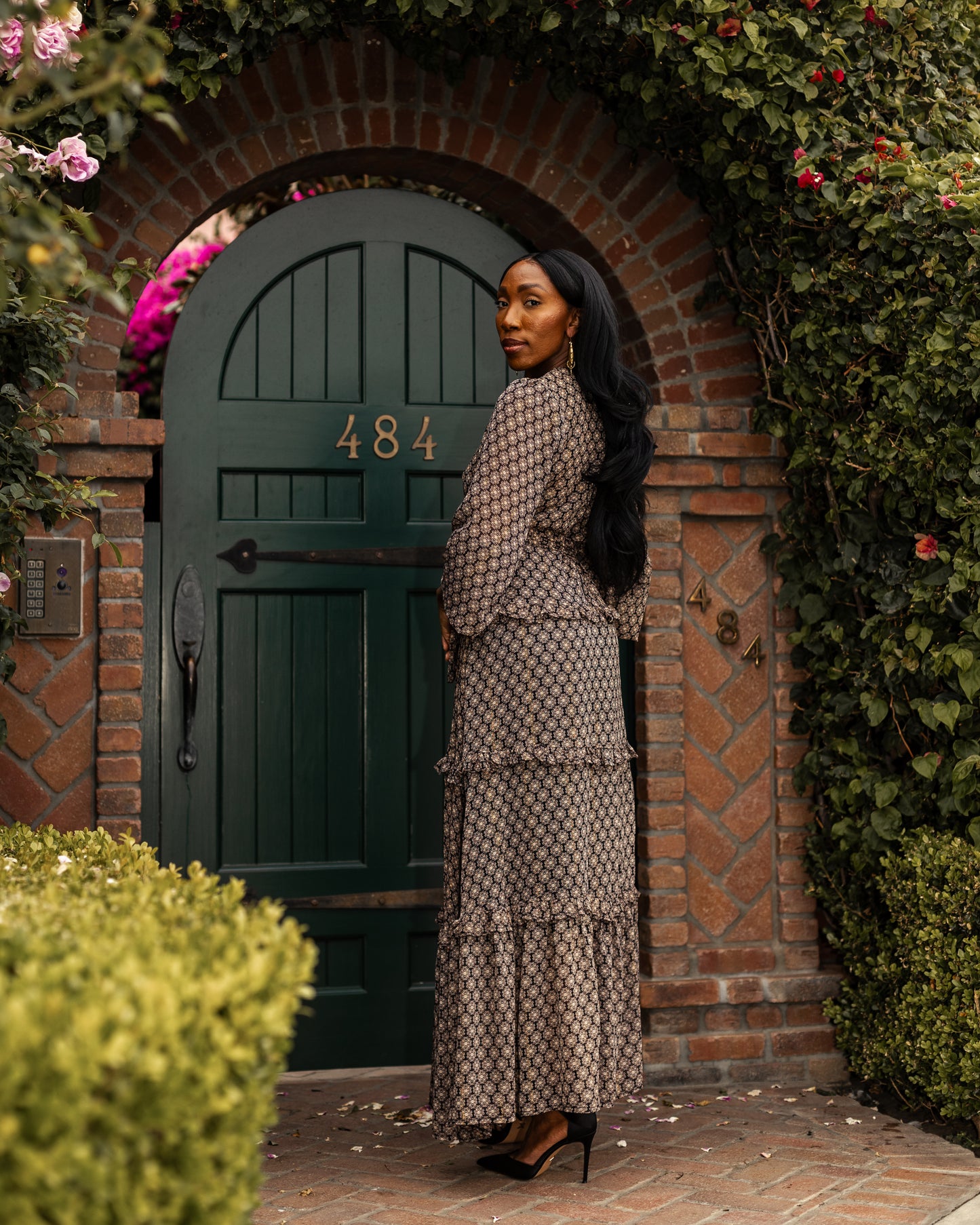 This beige and black floral maxi dress is crafted with a soft, metallic infused fabric, it features high neck, bishop sleeves, tiered ruffle skirt and matching sash for a cinched waist.