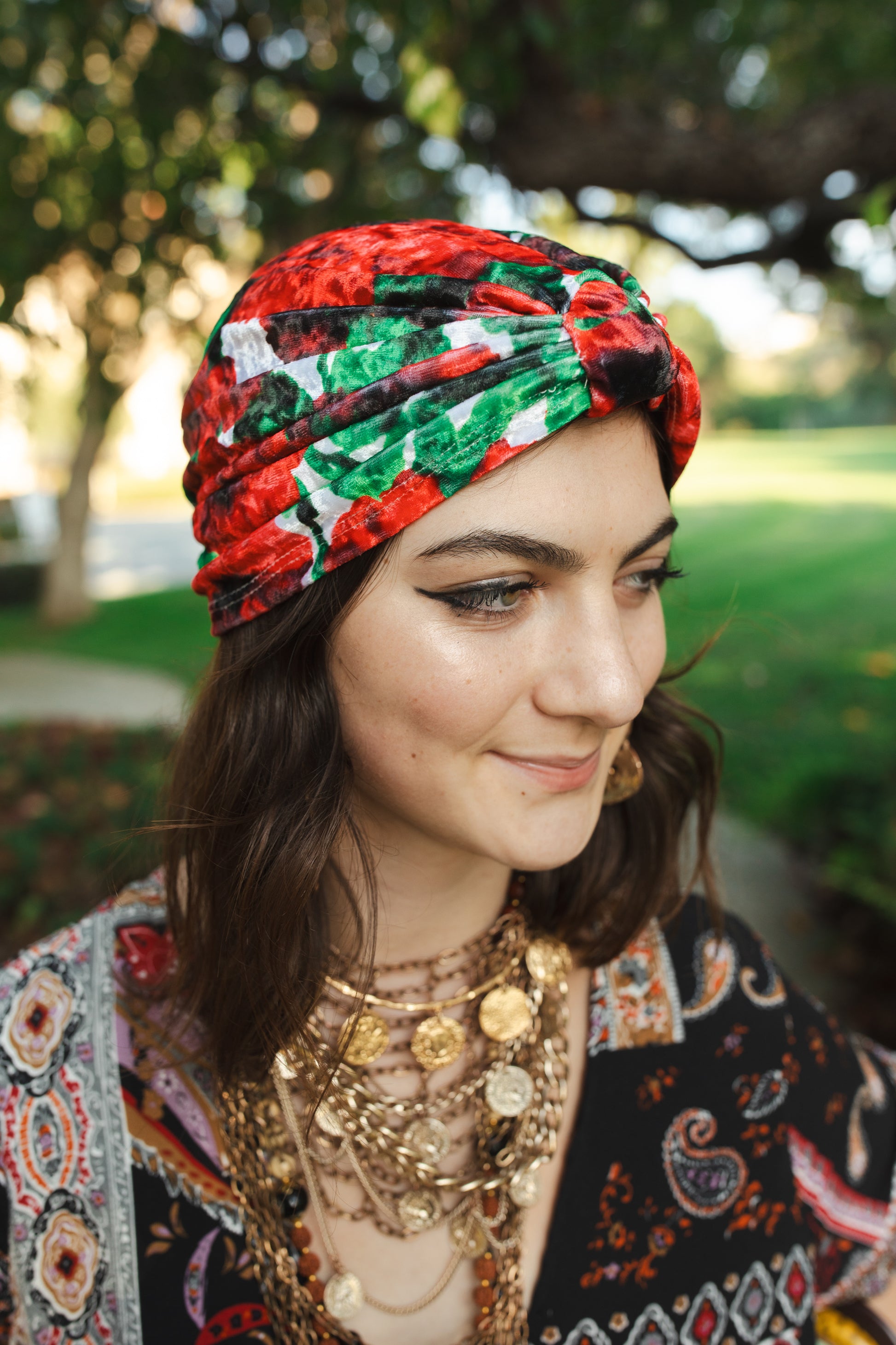 Red, green, white and black impressionist floral stretch velvet fashion turban hat that wears similar to a beanie, with ruching of the fabric that meets front and center at an elegant knot. Vintage-inspired retro 1920s mixed with a modern fabric.