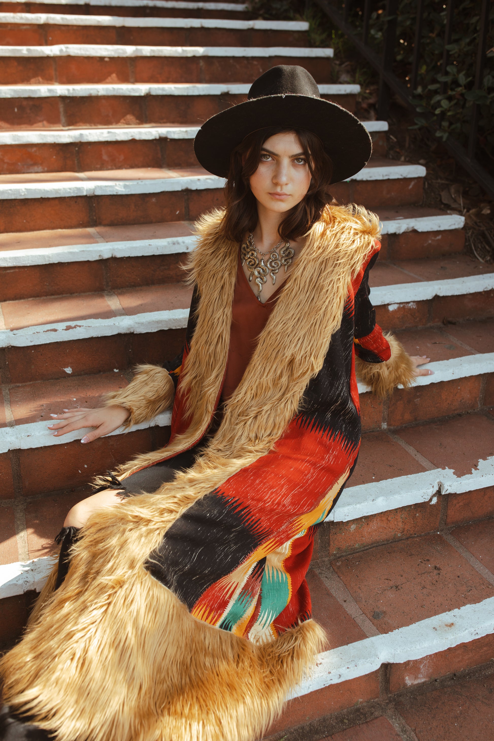 Long, penny lane style trench coat fashioned from a thick, abstract modernist colorblock print fabric featuring red, teal, yellow, black, and beige. Embellished with long tan faux fur along collar, lapel, cuffs, and hem. Retro bohemian color field art in style.
