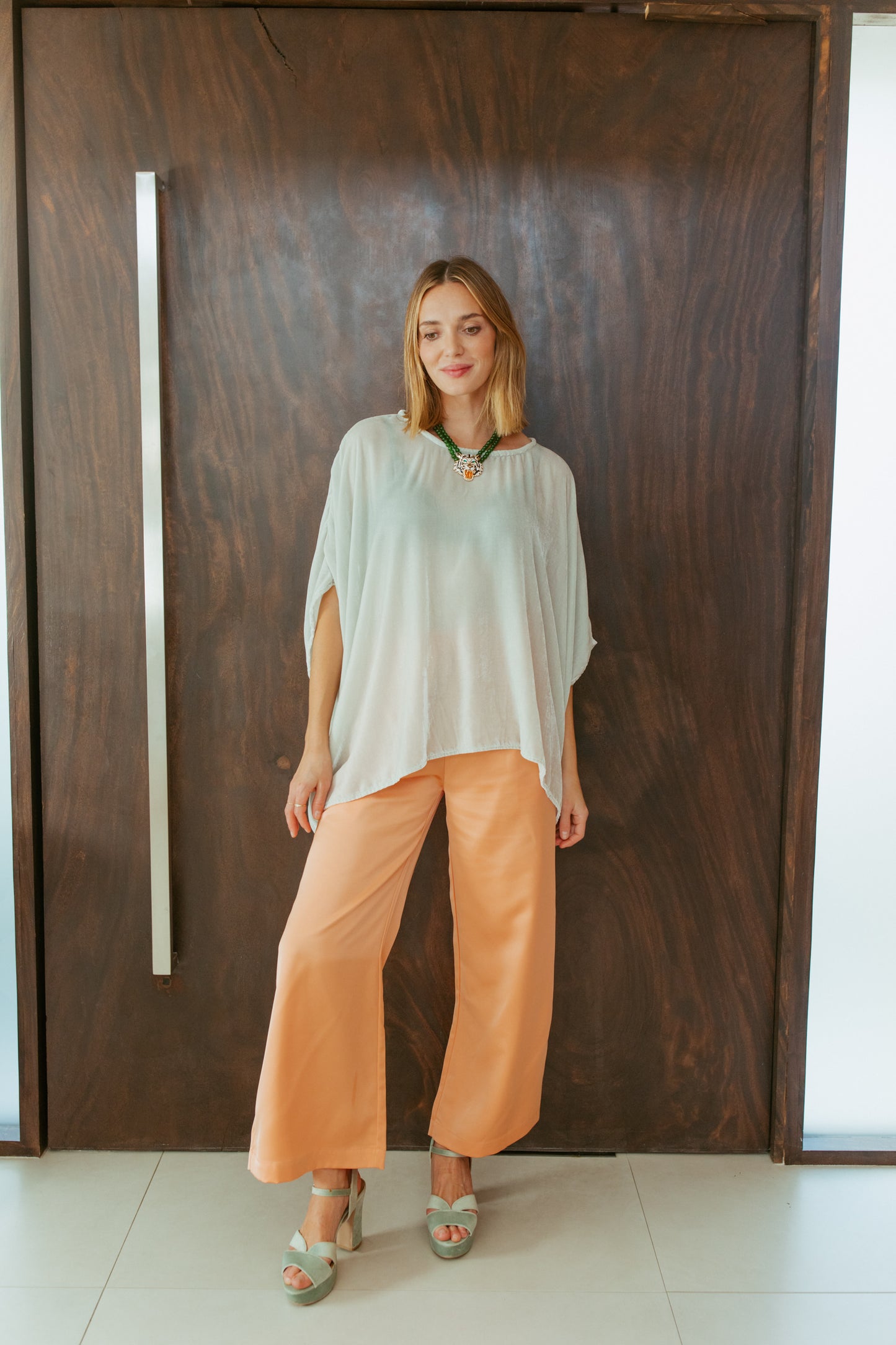 This pale sage green scarf top is a bohemian-inspired piece designed to drape elegantly on any shape. It features a boat neck, dolman sleeves, and a relaxed, flowy silhouette. Crafted with an incredibly soft silk velvet with a subtle shimmer that catches the light.