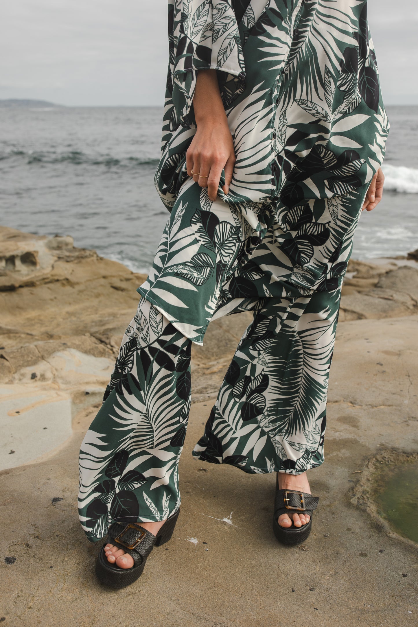 Midi length caftan tunic featuring white palm leaf print on dark hunter green. With v-neck, button up front, cutout at upper back with shoulder tie, and matching palazzo pant. Tropical bohemian chic aesthetic.