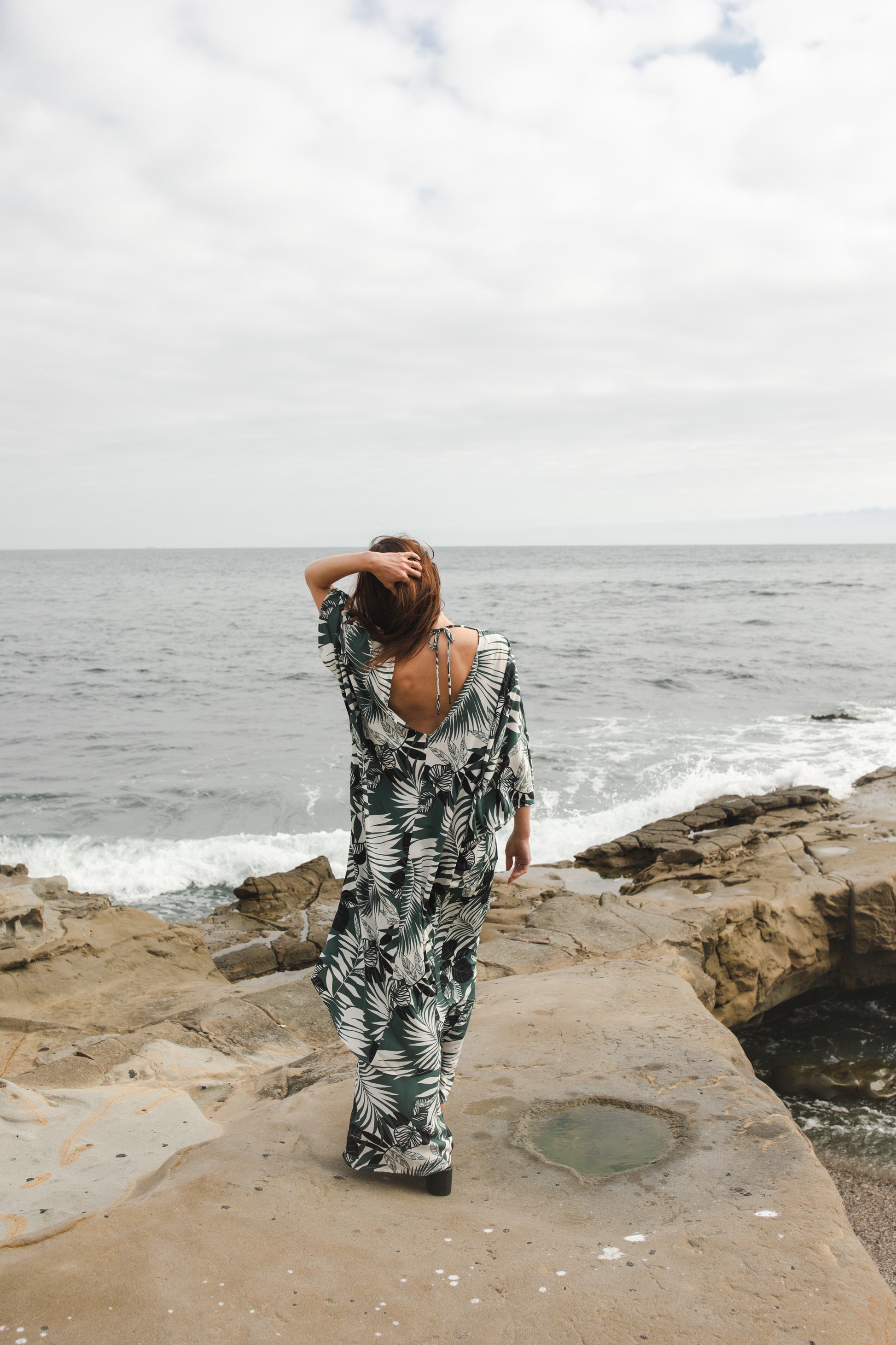 Midi length caftan tunic featuring white palm leaf print on dark hunter green. With v-neck, button up front, cutout at upper back with shoulder tie, and matching palazzo pant. Tropical bohemian chic aesthetic.