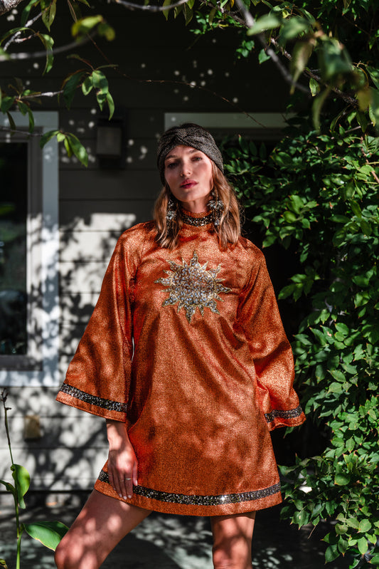 Crafted from a shimmering, fiery orange fabric embellished with an intricate sequin sun and matching sequin details at collar, cuffs, and hem, this is the bold and dreamy 60s revival romance dress every wardrobe craves