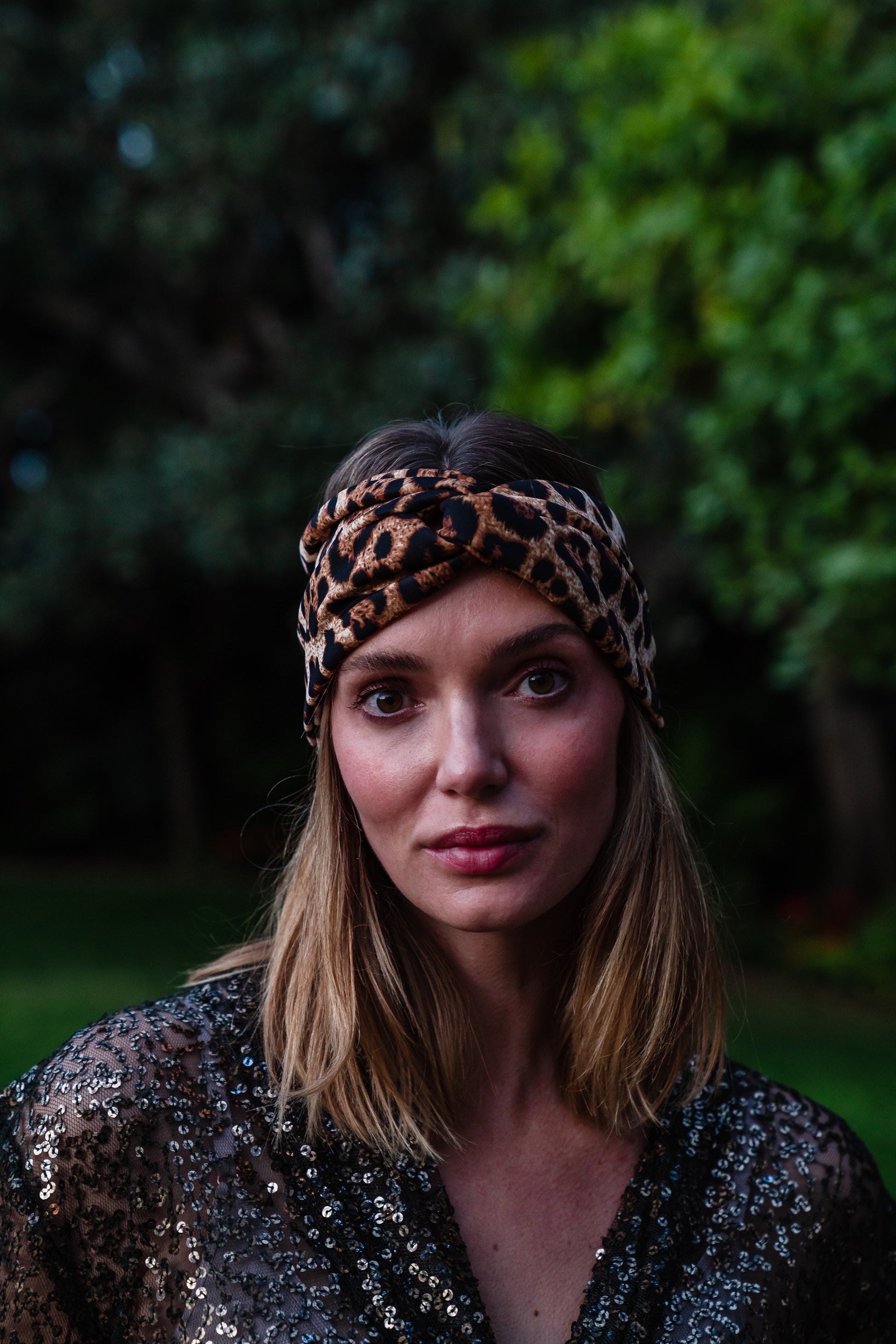 Jennafer Grace headband in leopard print. Headband is wide with twist detail in center. Easy to use to push back hair, or clip earrings on for a glamorous look. 