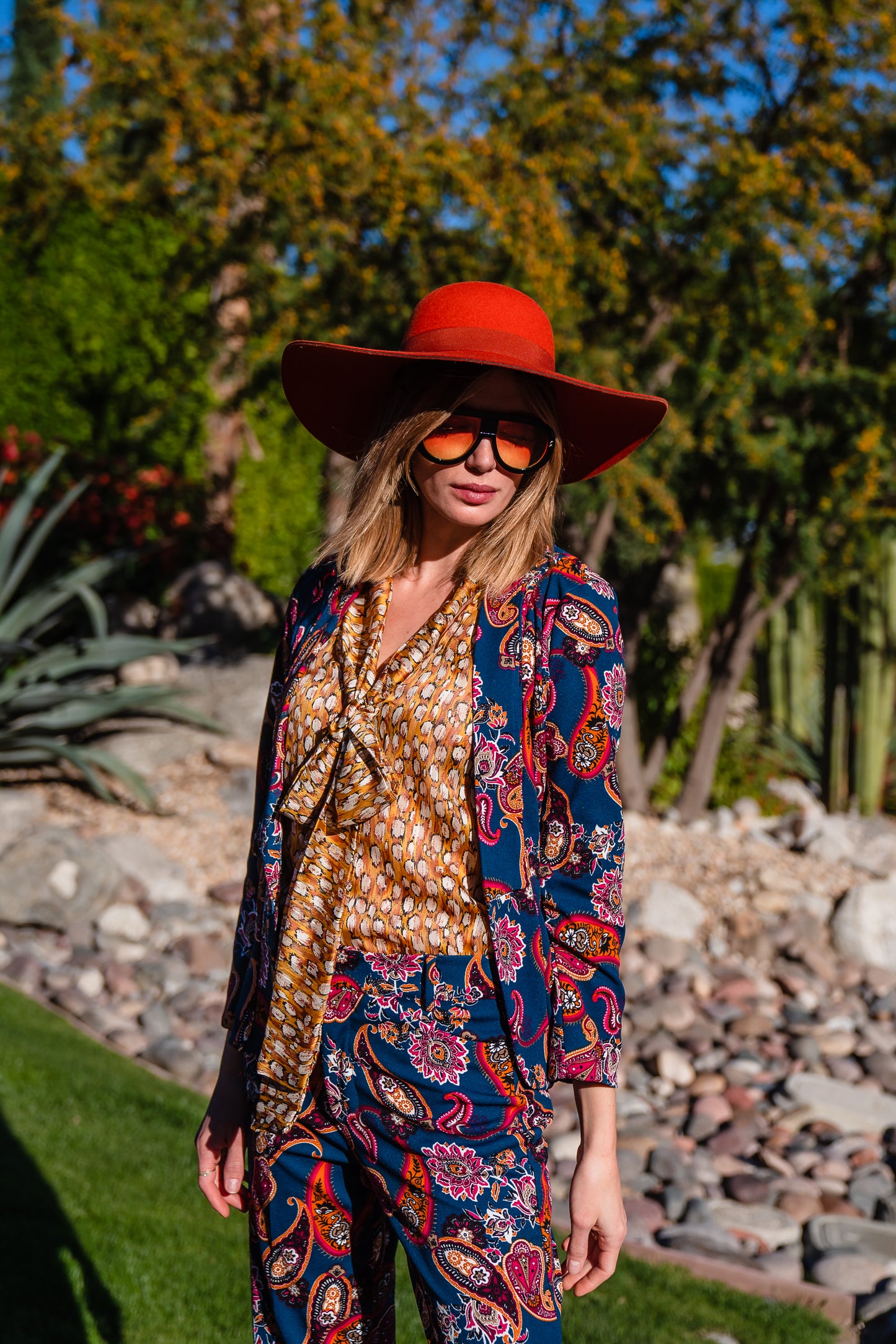 The Pepper Paisley Tuxedo Jacket. This retro glam suit jacket features a teal and rust paisley print. Has a wrist length arm hem, loose collar, and no button. 