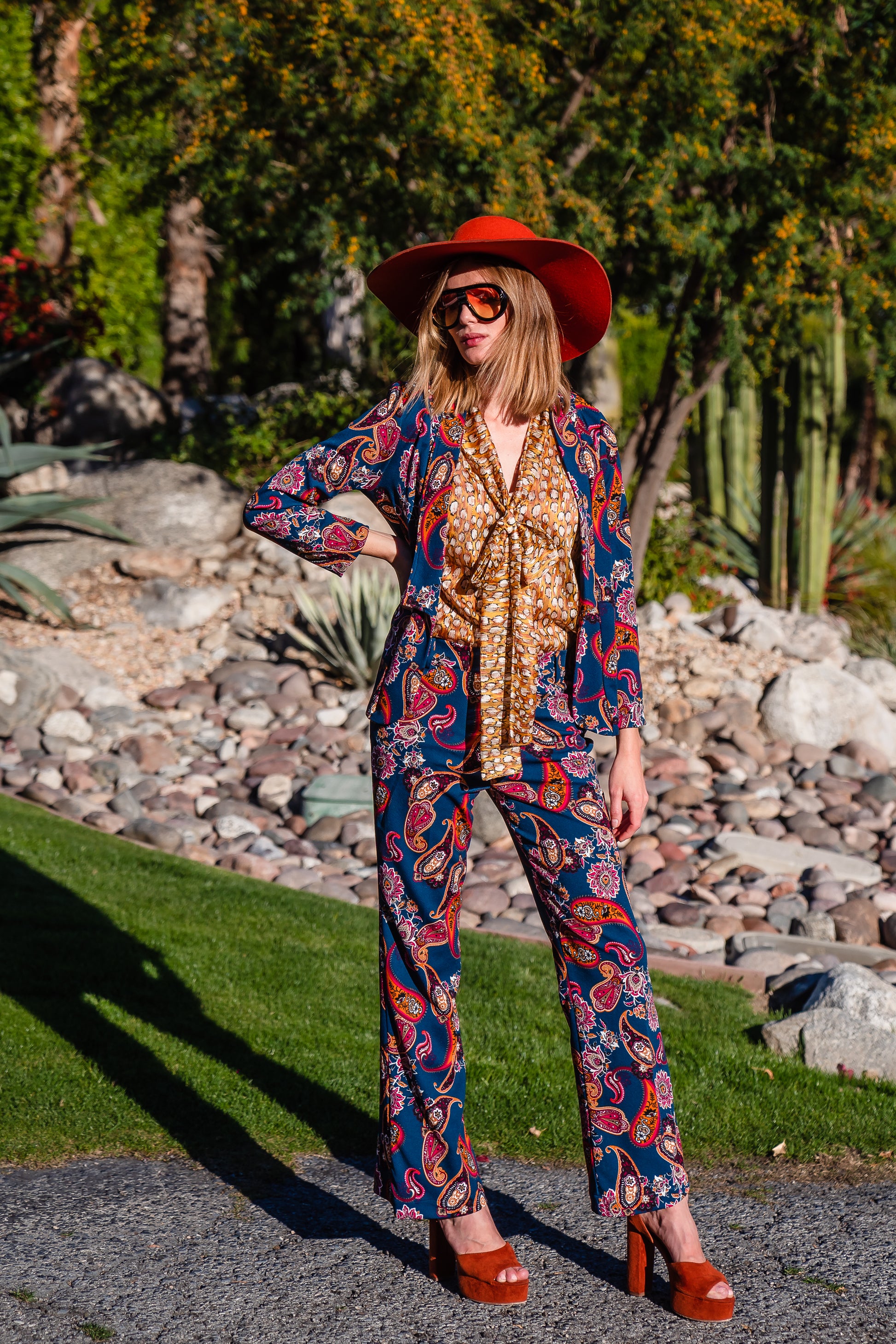 The Pepper Paisley Tuxedo Jacket. This retro glam suit jacket features a teal and rust paisley print. Has a wrist length arm hem, loose collar, and no button. 